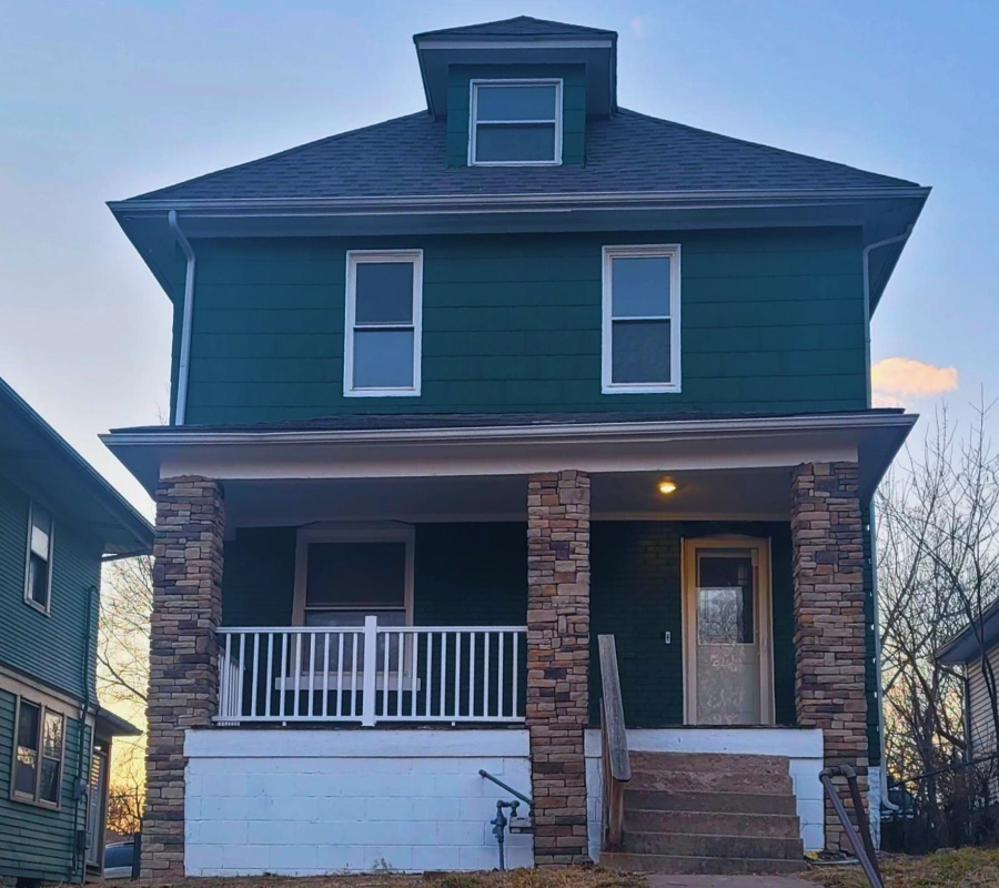 exterior home remodel stone pillars teal siding After photo of a home remodel featuring stacked stone porch pillars, new teal siding, and a fresh white porch railing